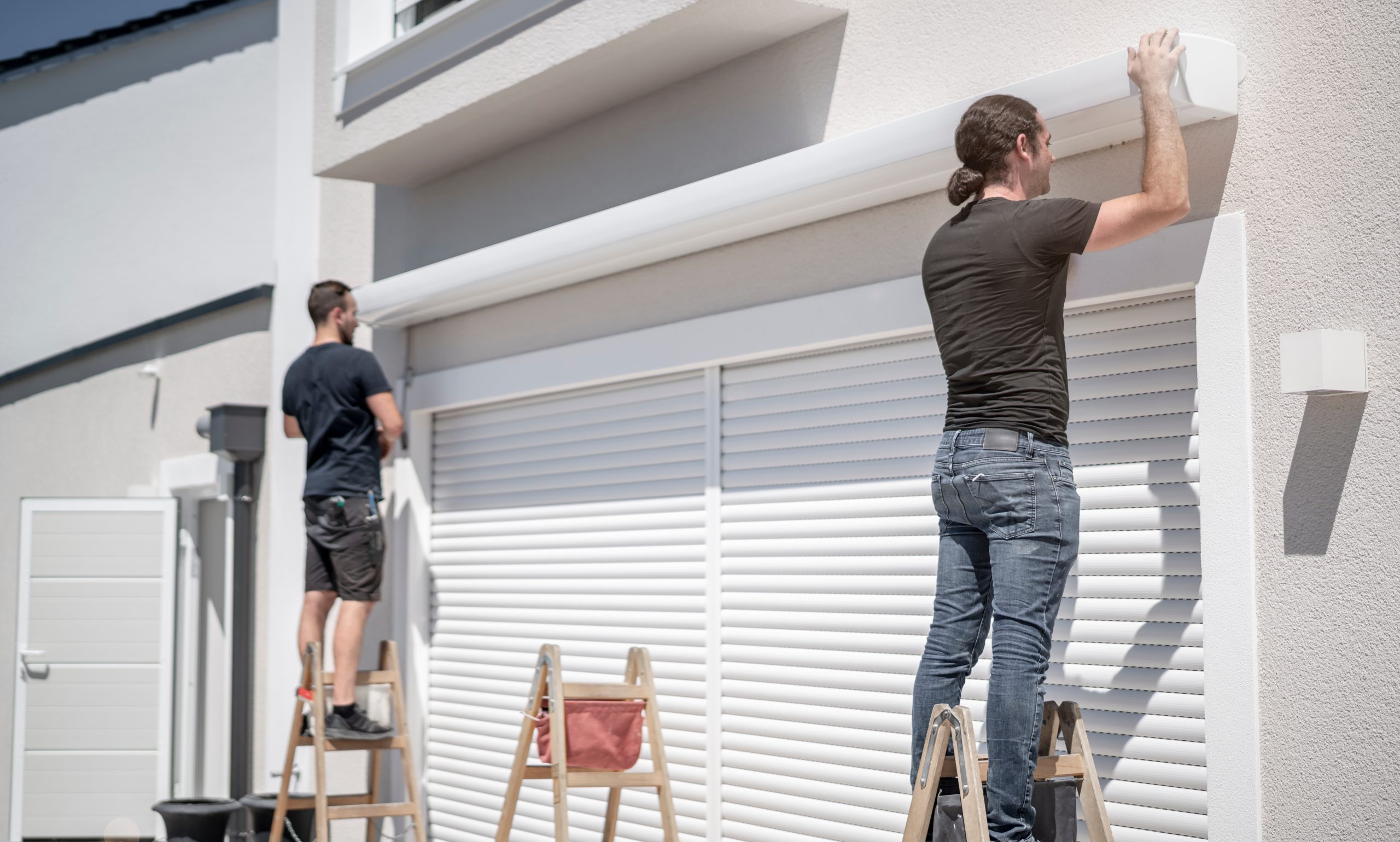 zwei Handwerker hängen eine Markise an den Halterungen an der Hauswand ein