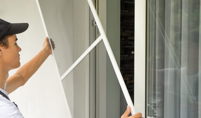 Young worker installing mosquito net wire mesh in plastic window frame. Protection from insects